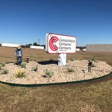 Landscaped sign for Consolidated Container Company with worker tending plants.