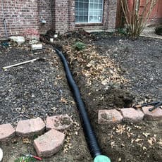 Drainage pipe installation in yard with exposed trench and landscaping.