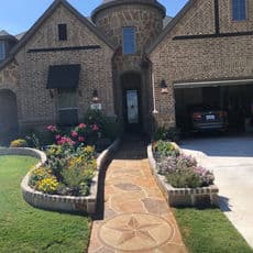 Beautiful brick home with stone walkway and colorful flower garden in front yard.