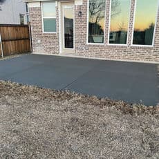 Newly poured concrete patio beside a residential home with large windows at sunset.