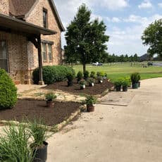 Front yard landscaping with flower beds, shrubs, and freshly laid mulch beside a brick house.