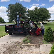 Landscaping crew using equipment to dig soil from a truck for garden maintenance.