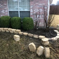 Landscaping project with stone edging and trimmed shrubbery next to a brick house.