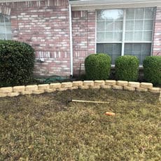 Garden bed with stacked stone edging, brown grass, and gardening tools nearby.
