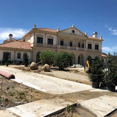 Luxury mansion with Mediterranean architecture, landscaped grounds, and construction in progress.
