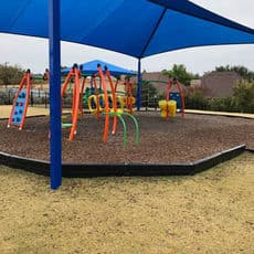 Colorful playground equipment under a blue shade canopy on a grassy field.