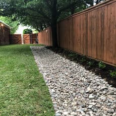 Stone pathway alongside a wooden fence in a lush green backyard.
