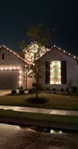 Festively lit house at night with colorful holiday lights and decorative landscaping.