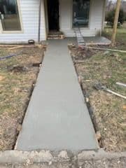Freshly poured concrete sidewalk leading to a house entrance, surrounded by unfinished landscaping.