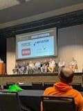 Panel discussion at a conference featuring multiple speakers and company logos on stage.