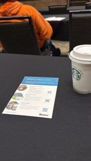 Starbucks coffee cup and event flyer on a table at a conference session.