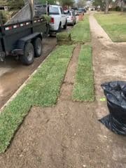 Freshly laid sod in a residential yard with trucks and landscaping materials nearby.