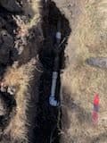 Underground pipe installation in a trench surrounded by dirt and grass.