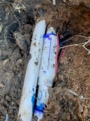 Damaged underground pipe with electrical wiring and blue fluid in the soil.
