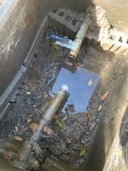 Water valve assembly in a dirty utility box with standing water and debris.