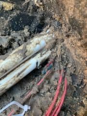 Buried damaged electrical cables with dirt and debris surrounding them.