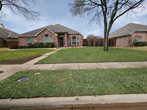 Single-story brick home with well-maintained lawn and trees, located on a quiet street.