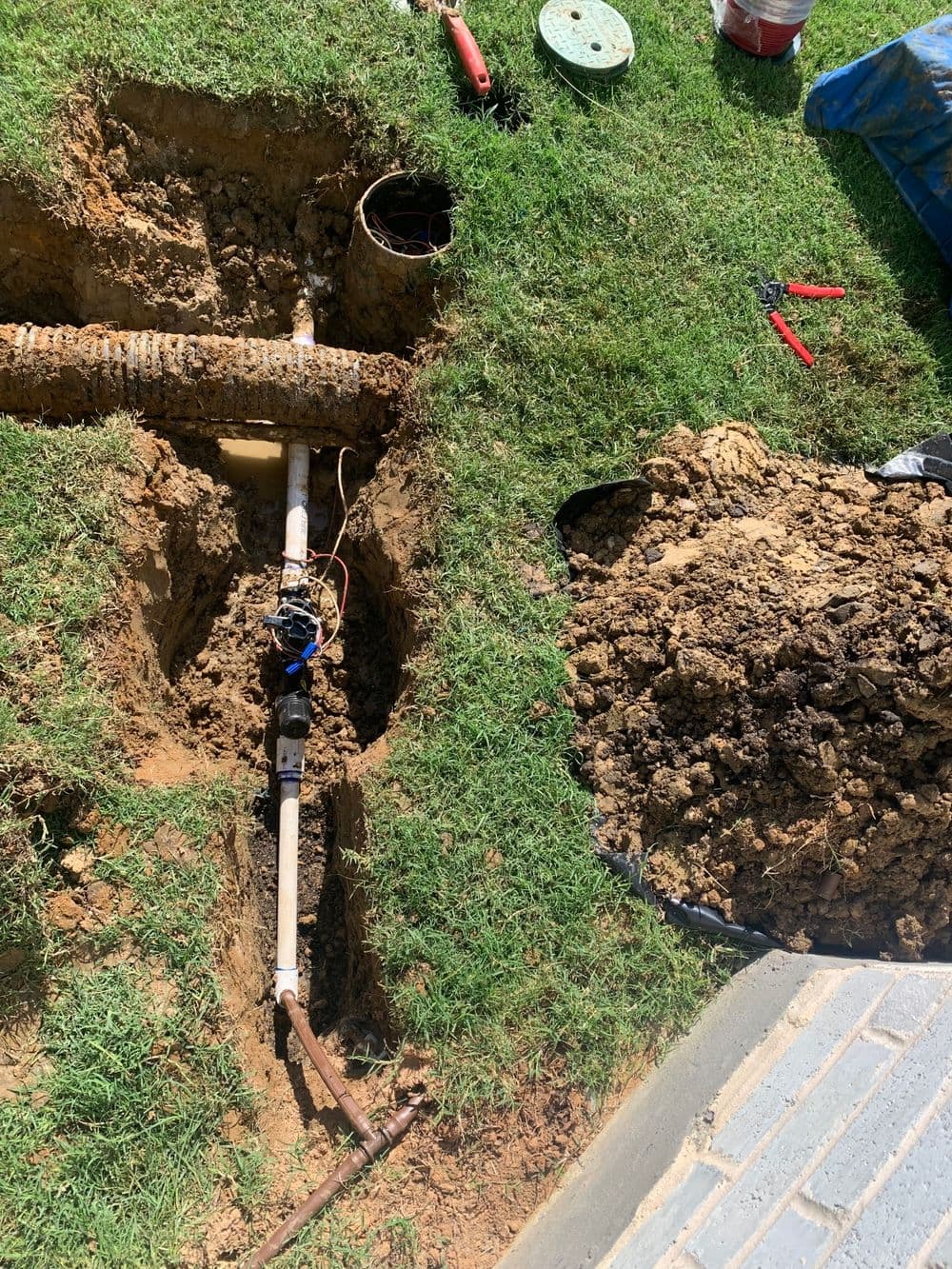 Excavated area showing a new pipe installation, tools, and mounded dirt in a yard.