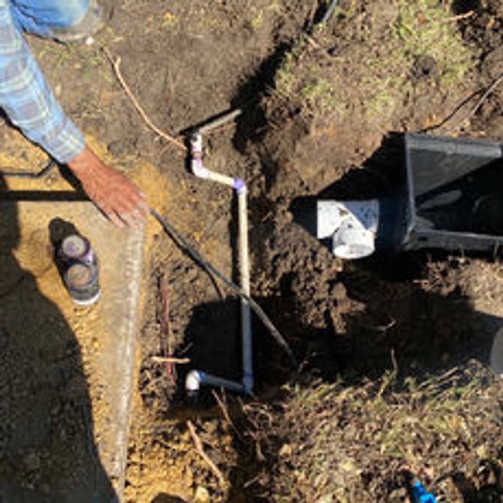Worker repairing pipes in a dug trench, showcasing plumbing tools and materials.