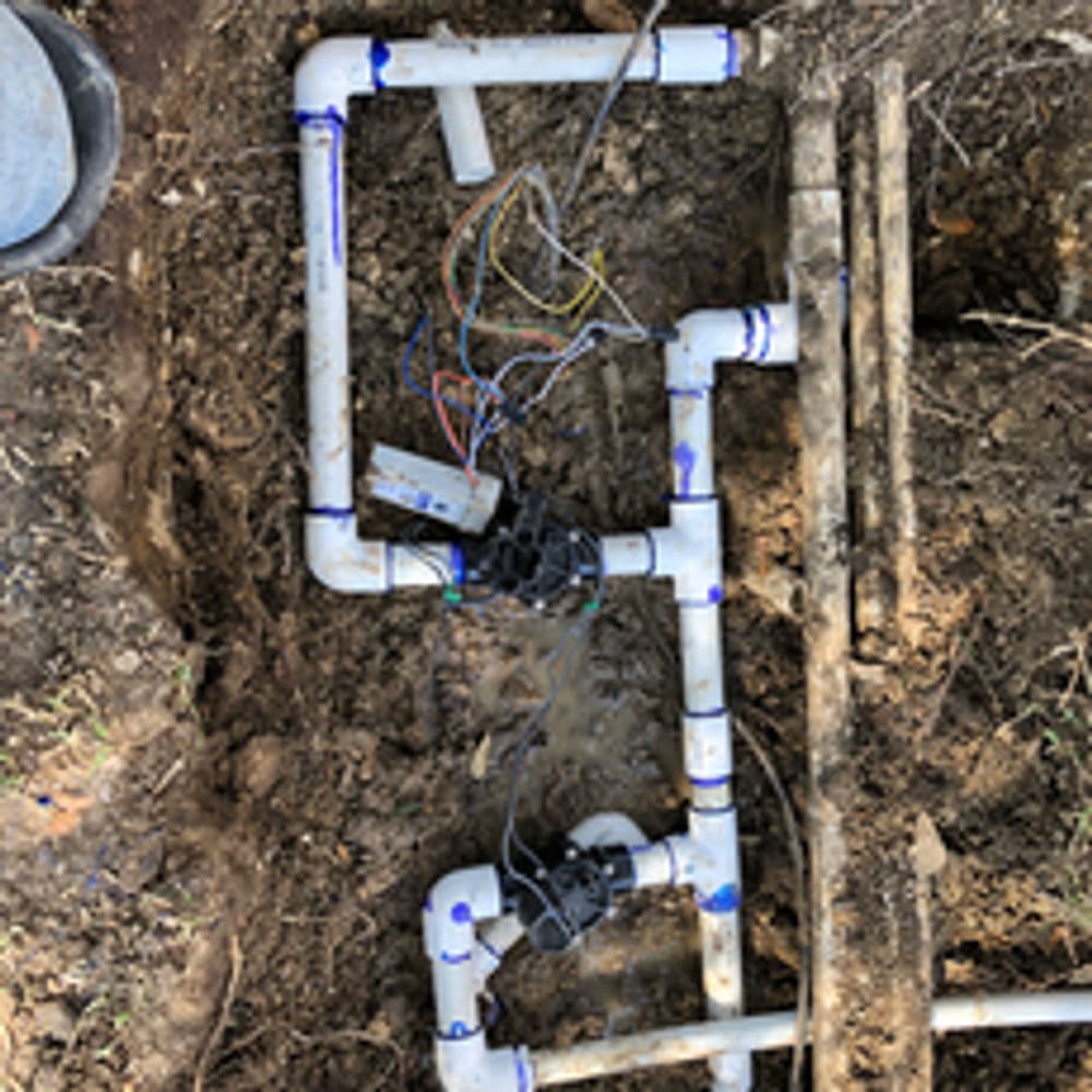 Irrigation system installation with PVC pipes and valve wiring in excavated soil.